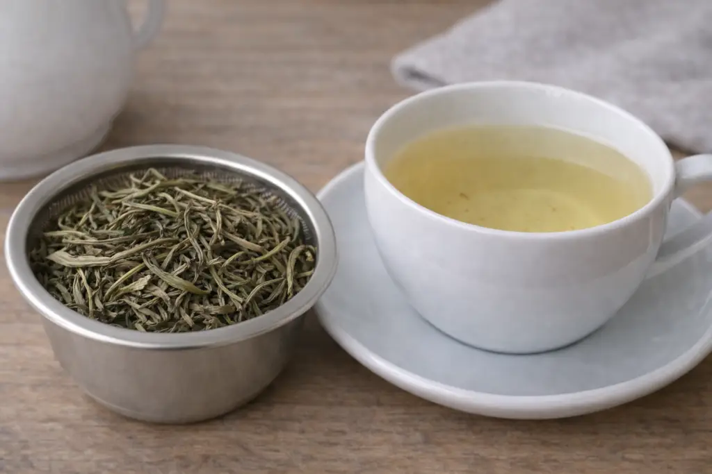 Infusion claire de thé blanc en feuilles dans une tasse en porcelaine